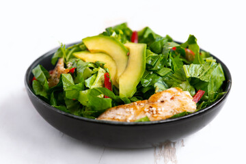 Healthy  vegetable buddha bowl salad with fried chicken and avocado, peppers and leaf lettuce on a white plate.