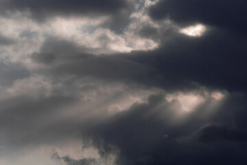 Wieczorne niebo pokryte ciemnymi, poszarpanymi chmurami. Pomiędzy chmurami przedostają się smugi światła słonecznego zabarwiając chmury na czerwony kolor. - obrazy, fototapety, plakaty