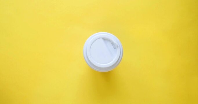 Craft paper coffee cup fills with drink and woman's hand take it. Coffee to go in a cup with a white lid on a yellow background. Looped 4K stop motion animation