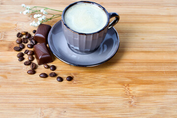 Chocolate praline, coffee beans and a cup of coffee on a wooden plate