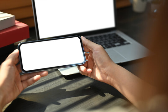 Mockup image of woman hands using smart phone at working desk front of laptop computer. Blank screen for advertising text