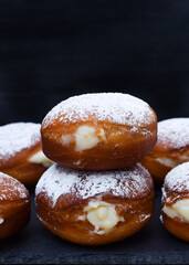 Bolas de masa dulce frita rellenas de crema con azúcar glas por encima, sobre plato de pizarra...