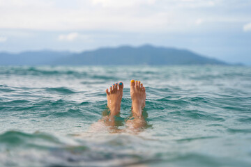 A girl with a yellow and blue pedicure relaxes in the sea overlooking the island