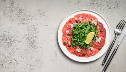 Beef carpaccio with capers, arugula and parmesan on a white plate, top view, copy space