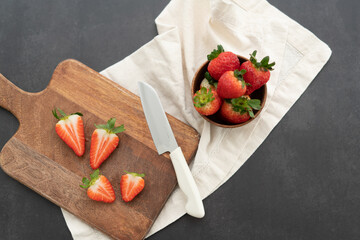Sliced strawberries on a cutting board with a bowl of strawberries