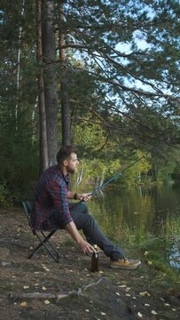 a man fishes and drinks beer sitting on the shore, vertical video