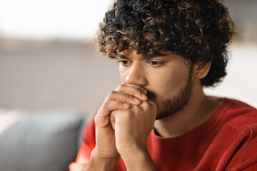 Fototapeta na wymiar Portrait Of Pensive Young Indian Man Sitting On Couch At Home