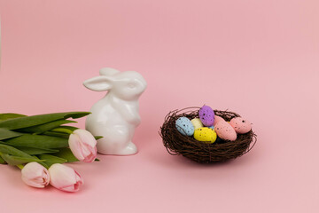 Easter card with rabbit toy, nest with eggs and bouquet of pink tulips, copy space. Pink background, flat lay