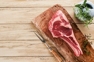 Fresh tomahawk raw steak. Dry aged raw tomahawk beef steak with herbs and salt on old wooden background. Preparing to grill.  Top view and copy space.