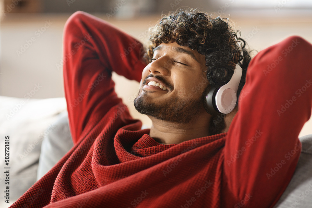 Sticker Smiling Young Indian Man Listening Music In Wireless Headphones At Home