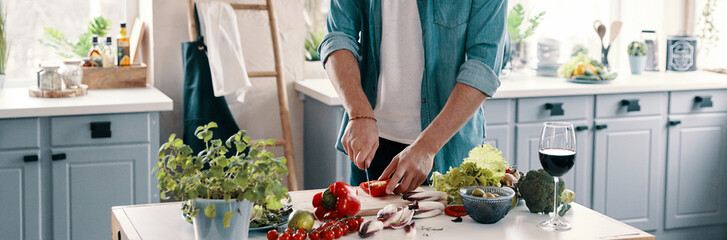 Close-up of unrecognizable man cutting vegetables while standing at the kitchen counter