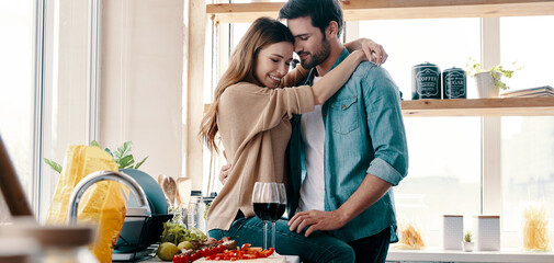 Beautiful young couple embracing while spending time at the domestic kitchen together