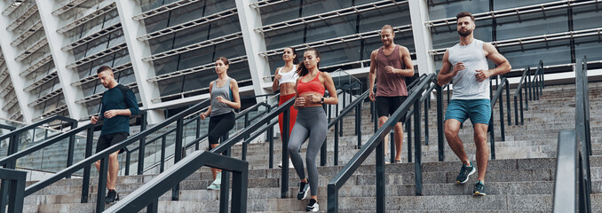 Group of young people in sports clothing running down the stairs outdoors together