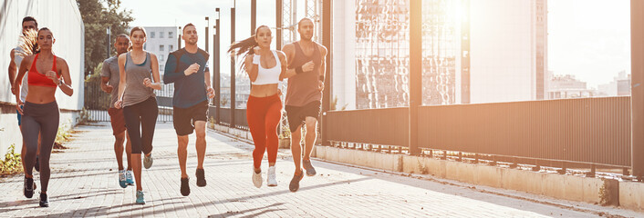 Full length of young people in sports clothing jogging outdoors together