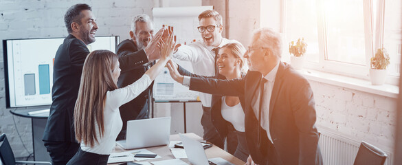 Group of happy business people giving high five while standing in board room in office