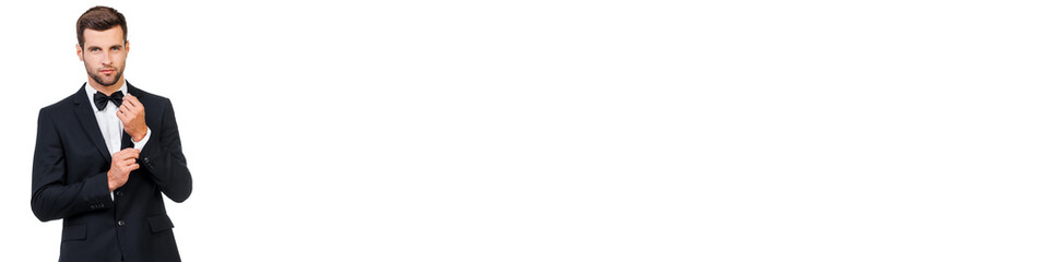 Handsome young man in suit and bow tie adjusting his sleeve against white background