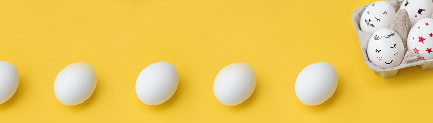 Easter Banner of white chicken eggs in row on yellow background. Painted eggs in paper tray in corner of photo. View from above. Copy space