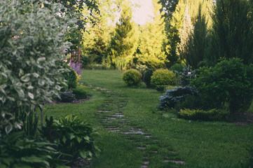 Evening summer walk in garden with curvy stone pathway and wooden archway. Natural woodland cottage...
