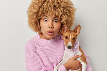 Shocked female pet owner stares at camera with omg expression poses with breed dog cannot believe...