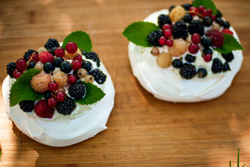 pavlova cakes with summer berries and fruits on a wooden board