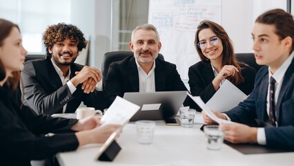 Successful businesspeople sitting at the table in conference room. Smiling office workers discuss new company strategy. 