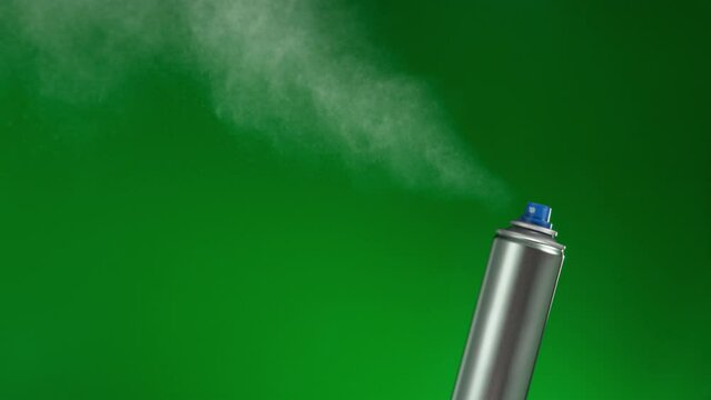 Silver mock-up spray can on green background sprays fountain of vaporized foam particles. stabilized locked shot. Concept backplate with copy space for product showcase.