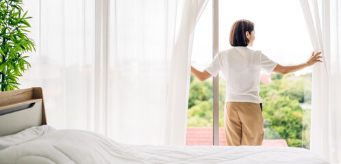 Happy young beautiful pretty asian woman waking up and opening window curtains.Girl feeling...