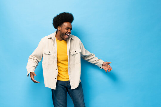 Surprised Afro African American man smiling with open hand gesture in light blue color studio shot isolated background