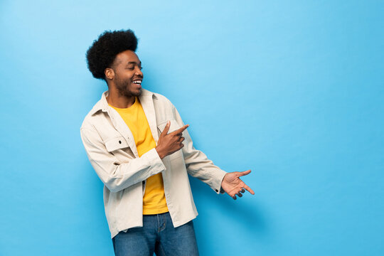 Surprised Afro African American man smiling with hands pointing to copy space aside in light blue color studio shot isolated background