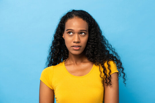 Portrait of mixed race African woman thinking with eyes looking up in light blue studio isolated background