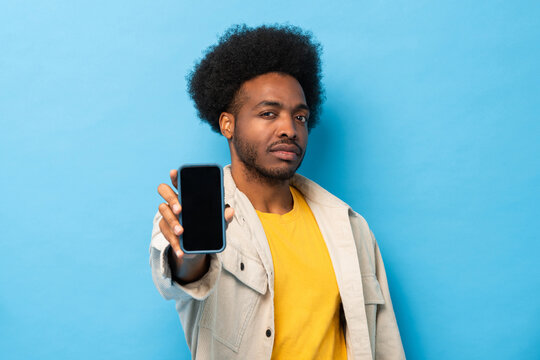 Afro African-American man showing empty screen mobile phone in isolated light blue color studio background