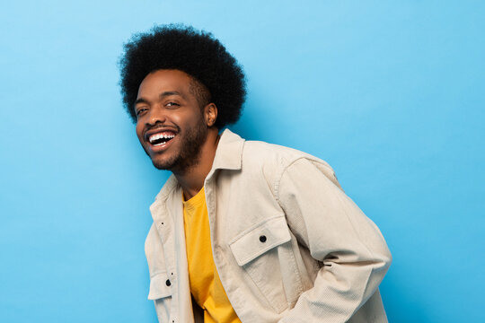 Happy positive Afro African American man laughing and looking at camera in light blue isolated background studio shot