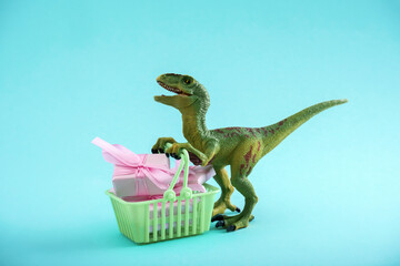 Funny green dinosaur toy with shopping basket full of present boxes on a blue background. Sale...