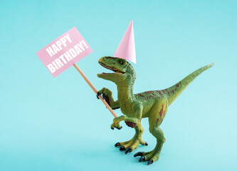 Naklejka premium Cute dinosaur in birthday hat holding Happy Birthday sign on blue background. CUte birthday greeting card idea concept.