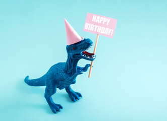Cute dinosaur in birthday hat holding Happy Birthday sign on blue background. Cute birthday greeting card idea concept.
