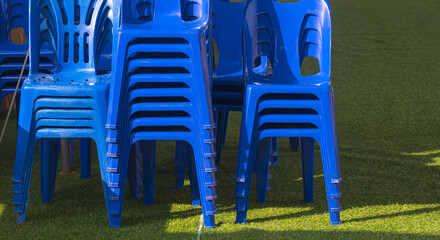 Many stack of blue plastic chairs on green artificial turf for outdoors event