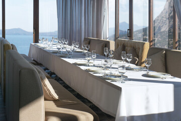 Full serving table waiting for guests. Restaurant indoors room with mountains and sea view. Luxury space for banquet, dinner, feast, party.