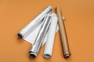 Rolls of aluminium foil and baking paper on orange background