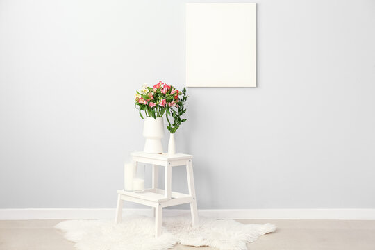 Vase with beautiful alstroemeria flowers and candles on step ladder near light wall
