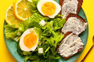 Plate of delicious salad with boiled eggs and cream cheese sandwiches on yellow background