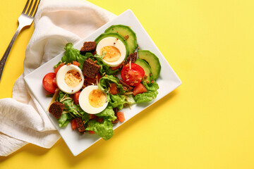 Plate of delicious salad with boiled eggs and salmon on yellow background