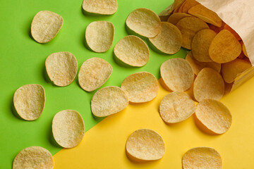 Overturned paper bag with delicious potato chips on green and yellow background