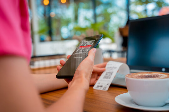 Woman using contactless payment by mobile phone with QR code at cafe