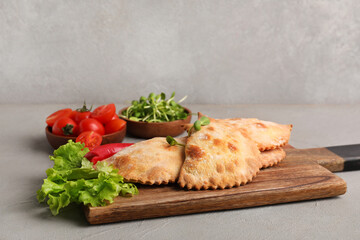 Wooden board with baked meat empanadas, lettuce, microgreen and vegetables on grunge background