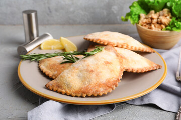 Plate with baked meat empanadas and rosemary on grunge background, closeup