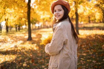 Student girl wearing coat and hat in autumn park. Beautiful autumn teen lady with autumn leaves on fall nature background