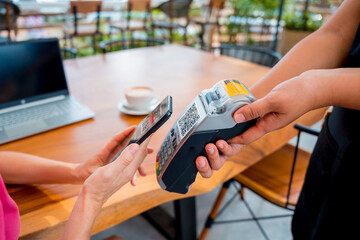 Woman using contactless payment by mobile phone with QR code at cafe