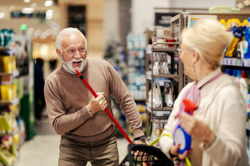 A playful old man is singing with mop at the supermarket and having fun.