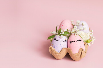 Banner. Stylish Easter pink and liliac eggs with cute faces in floral wreath crowns in carton tray on pink background. Easter decorations and gift. Happy Easter concept. Copy space. Isolated.