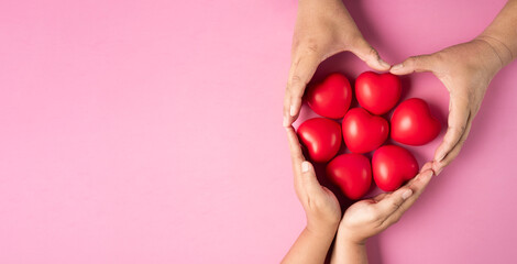 Adult hands around red heart on pink background , health care, organ donation, family life...